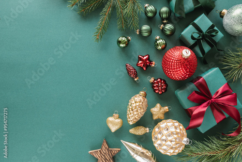 Overhead view of Christmas ornaments, wrapped gifts, fir branches on green background.