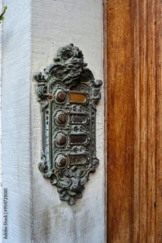 Old vintage, sculpted and decorated boor buzzer or intercom on an outside wall next to entry door. Close up shot, no people