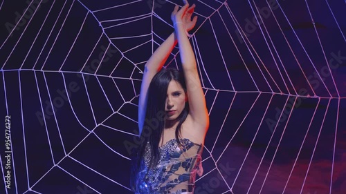 sexy woman victim of spider hanging tied on huge web. fantasy girl gothic dark queen in evening dress. dark studio creative scenery design. performance show night club celebration party halloween