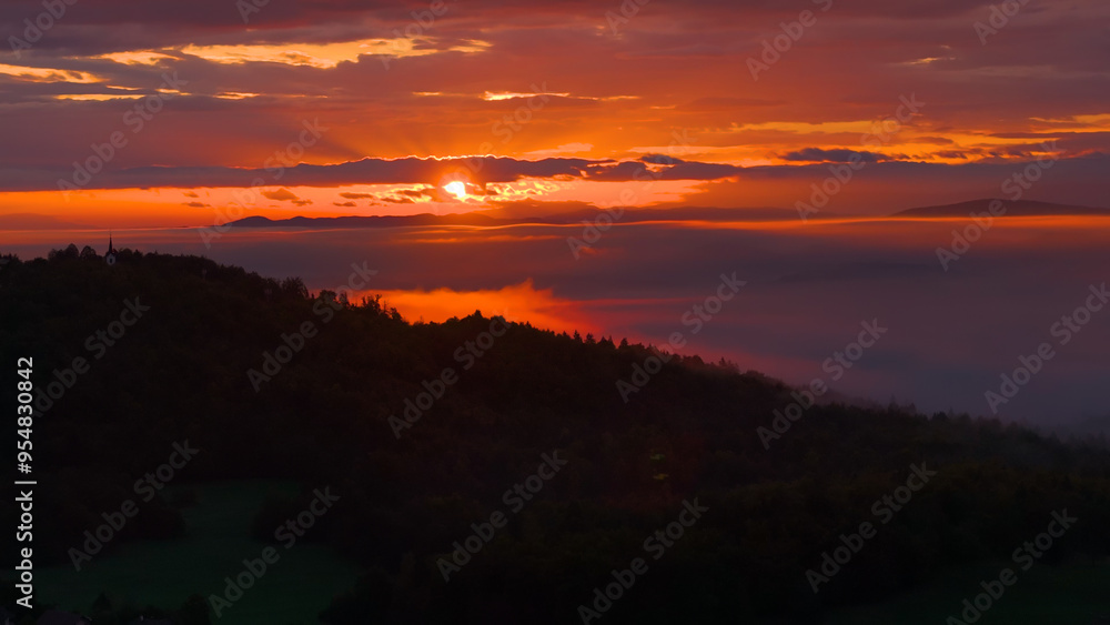 LENS FLARE, SILHOUETTE: A serene sunset over misty hills and valleys, with vibrant colours lighting up the sky. Ethereal view of hilly landscape under colourful clouds as the day transitions to night. LENS FLARE, SILHOUETTE: A serene sunset over misty hills and valleys, with vibrant colours lighting up the sky. Ethereal view of hilly landscape under colourful clouds as the day transitions to night.