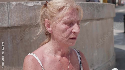 Blonde woman in her sixties wipes sweat in the heat outdoors photo