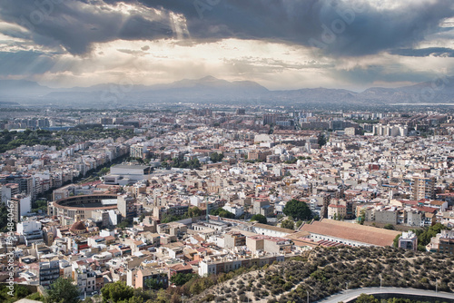 A panoramic view of Alicante, one of Spain's largest cities, showcasing its expansive urban landscape beneath a partly cloudy sky, offering a picturesque and vibrant scene. #954840467