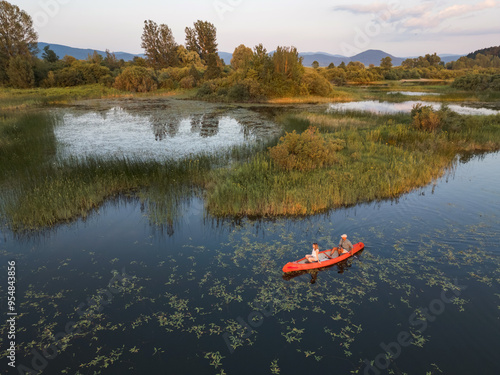 Couple enjoying romantic traveling with a canoe on the calm lake during summer sunset, aerial shot. Outdoor wellness concept. photo