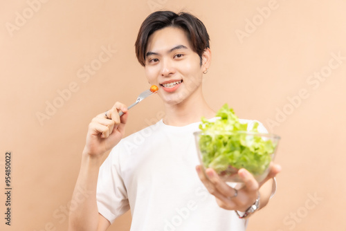 A happy asian people in white shirts, holding glasses of milk and a bowl of salad, against a beige background.