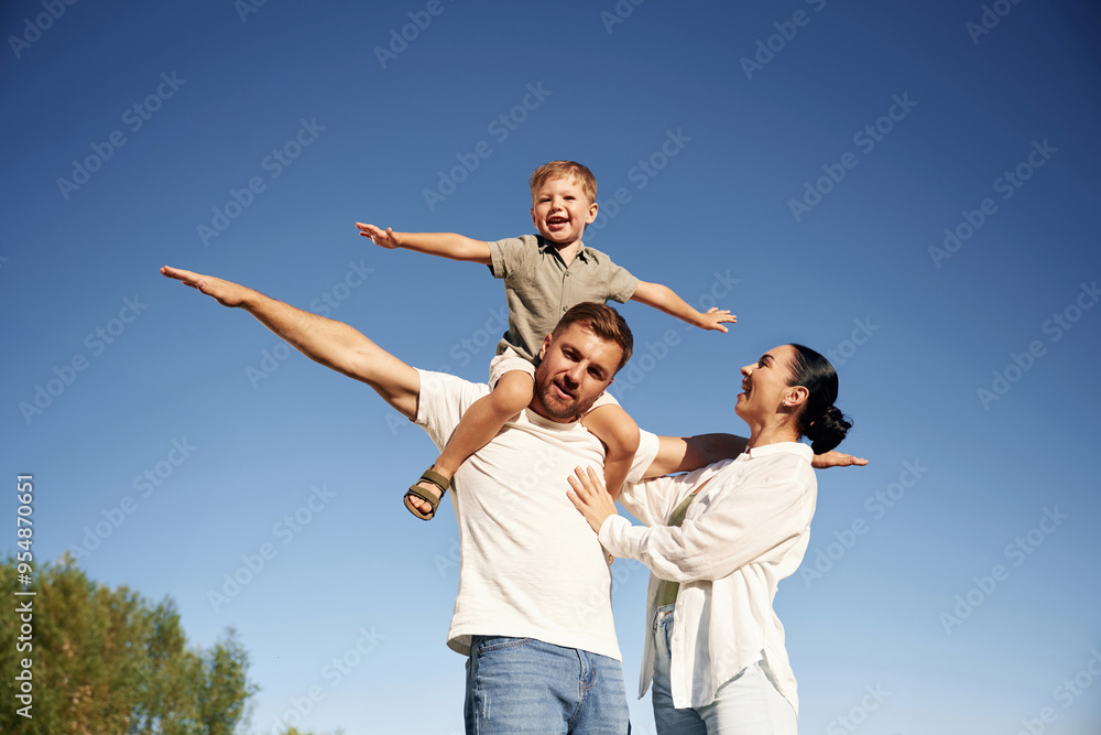 Hands to the sides, flying, imagination. Mother and father are with son outdoors on the field Hands to the sides, flying, imagination. Mother and father are with son outdoors on the field