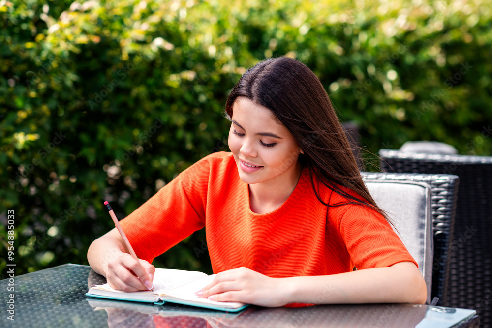 Photo of pretty teen good mood girl sit table cafe write notebook wear red clothes walk outside urban city park Photo of pretty teen good mood girl sit table cafe write notebook wear red clothes walk outside urban city park