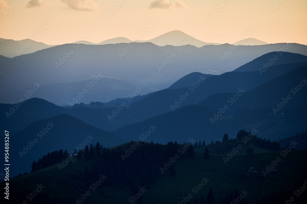 Fototapeta premium Soft blue hues of layered mountain ranges stretch into the distance under evening sky, creating tranquil and atmospheric landscape filled with gentle gradients and sense of vastness.