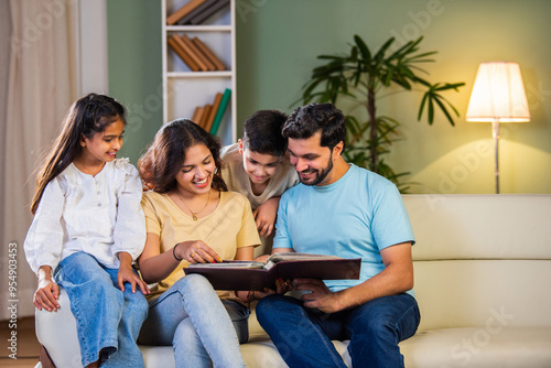 Canvas Print Happy Indian family of four relaxing on a sofa, reading books Or viewing photo a