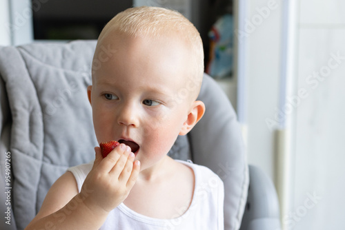 Little child with rash on the cheeks eating strawberry.