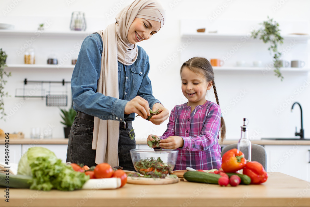 Muslim mother and daughter chop, tear greens in salad bowl. They enjoy family time together while preparing vegetables in bright modern kitchen, showcasing healthy eating and lifestyle. Muslim mother and daughter chop, tear greens in salad bowl. They enjoy family time together while preparing vegetables in bright modern kitchen, showcasing healthy eating and lifestyle.