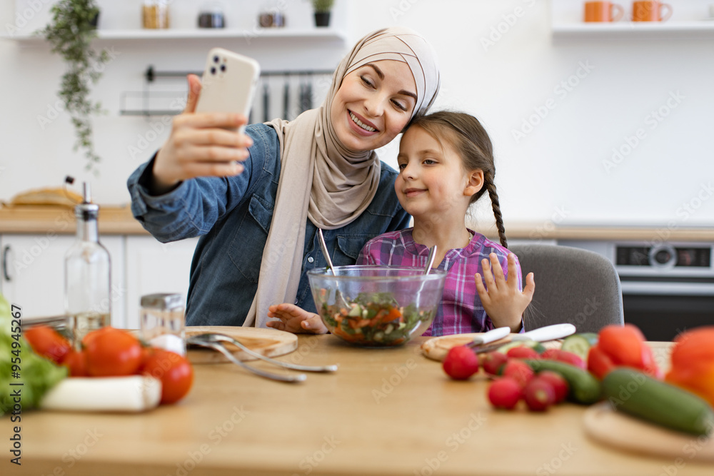 Bonding moment emphasizing healthy eating, family connection, and modern technology. Muslim mother and daughter enjoying video call together showing healthy salad in a bright kitchen. Bonding moment emphasizing healthy eating, family connection, and modern technology. Muslim mother and daughter enjoying video call together showing healthy salad in a bright kitchen.