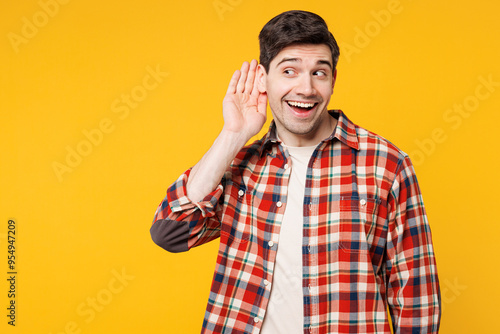 Young curious nosy happy fun man he wears red checkered shirt casual clothes try to hear you overhear listening intently isolated on plain yellow orange background studio portrait. Lifestyle concept.