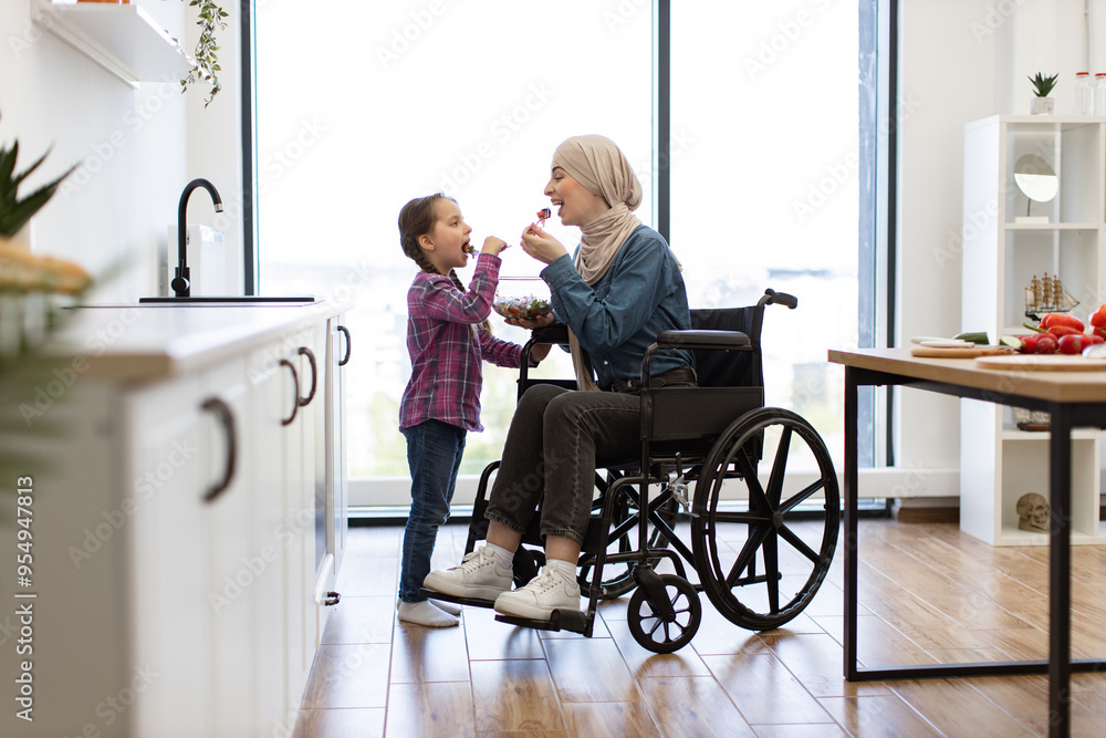 Concept of family bonding, inclusivity, healthy eating, and positive parenting. Muslim mother in wheelchair and daughter share fresh salad in kitchen. Young girl feeds mother with love and care. Concept of family bonding, inclusivity, healthy eating, and positive parenting. Muslim mother in wheelchair and daughter share fresh salad in kitchen. Young girl feeds mother with love and care.