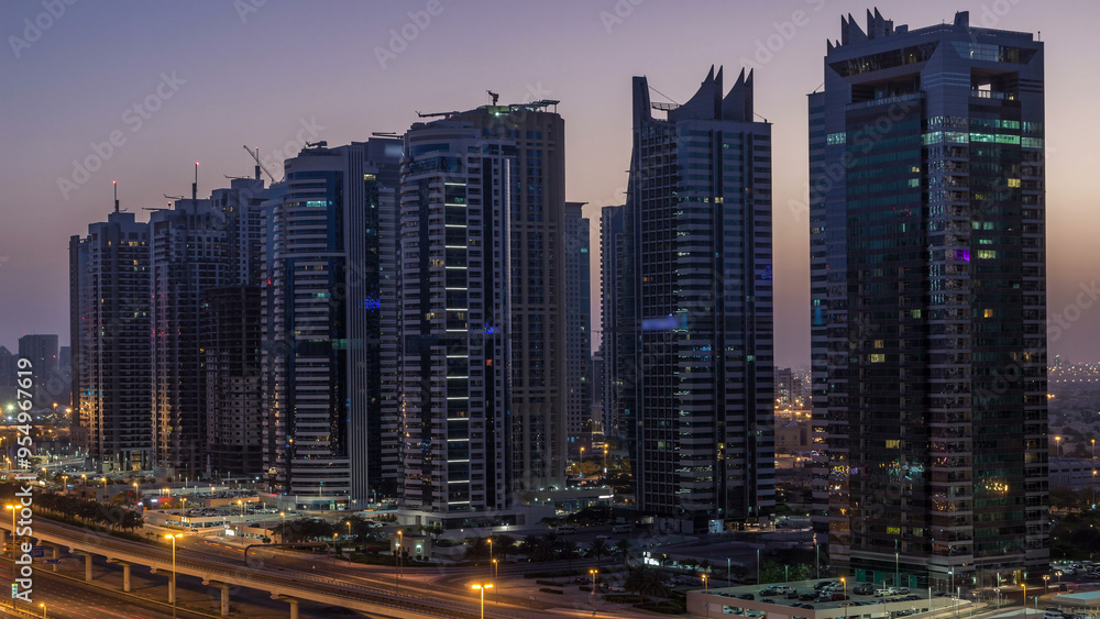Obraz premium Aerial view of Jumeirah lakes towers skyscrapers night to day timelapse with traffic on sheikh zayed road.