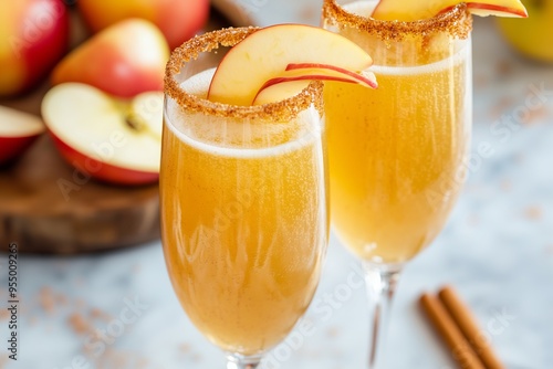 two caramel apple mimosas in champagne flutes, with a cinnamon-sugar rim and garnished with fresh apple slices