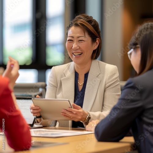 Business meeting in modern office with a smiling woman engaging with colleagues using a tablet while discussing project ideas