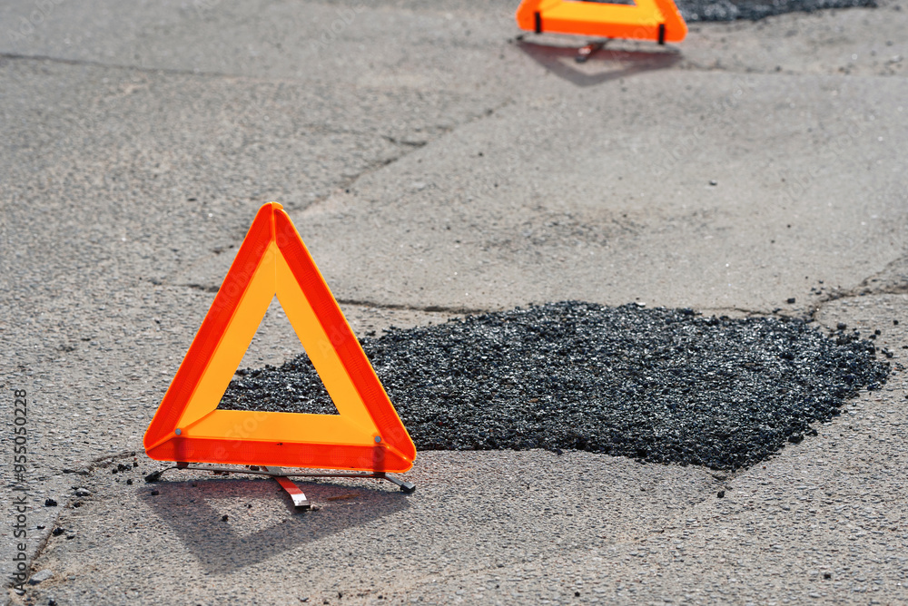 Fresh asphalt patch marked by warning triangle for safety. Roadwork. Patched asphalt road. Asphalt patch marked by warning triangle on city road, temporary road repair work.