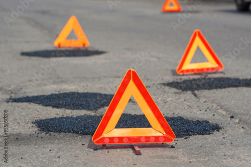 Patched asphalt road. Asphalt patch marked by warning triangle on city road, temporary road repair work. Fresh asphalt patch marked by warning triangle for safety. Road repair.