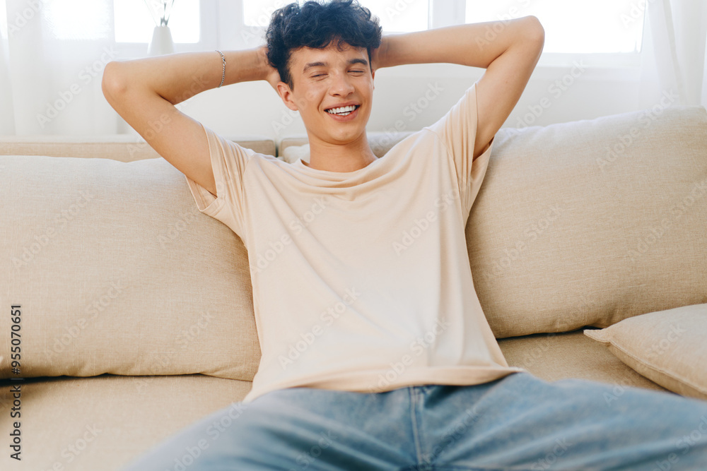 Young man relaxing on a sofa, smiling contently, casual outfit, light toned room, showcasing comfort and leisure in a cozy, modern living space Young man relaxing on a sofa, smiling contently, casual outfit, light toned room, showcasing comfort and leisure in a cozy, modern living space