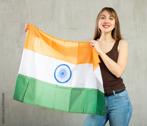 Portrait of happy woman posing with national flag of India in hands on gray background in studio photo