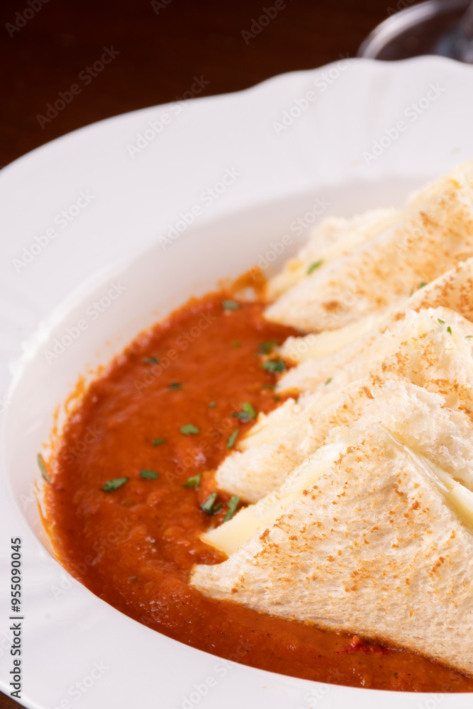 dish of cream tomato soup with melted cheese toast dipped in close-up with dish of cream tomato soup with melted cheese toast dipped in close-up with