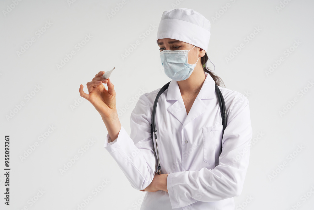 Doctor wearing face mask looking at measurement on medical thermometer over white background Doctor wearing face mask looking at measurement on medical thermometer over white background
