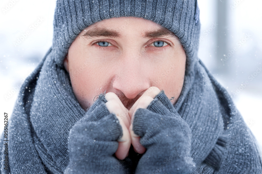 Handsome guy with blue eyes in a gray knitted hat outdoors. Close-up winter portrait. Snowflakes on eyelashes. Handsome guy with blue eyes in a gray knitted hat outdoors. Close-up winter portrait. Snowflakes on eyelashes.