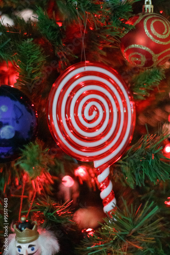 A close-up of a Christmas tree with a red and white swirl candy ornament, surrounded by festive lights and green branches.