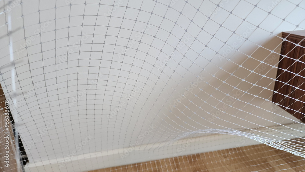 Netting is made of gray polypropylene, installed near white wall. Gray ...