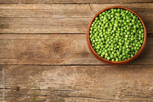 Fresh green peas in bowl on wooden table, top view. Space for text