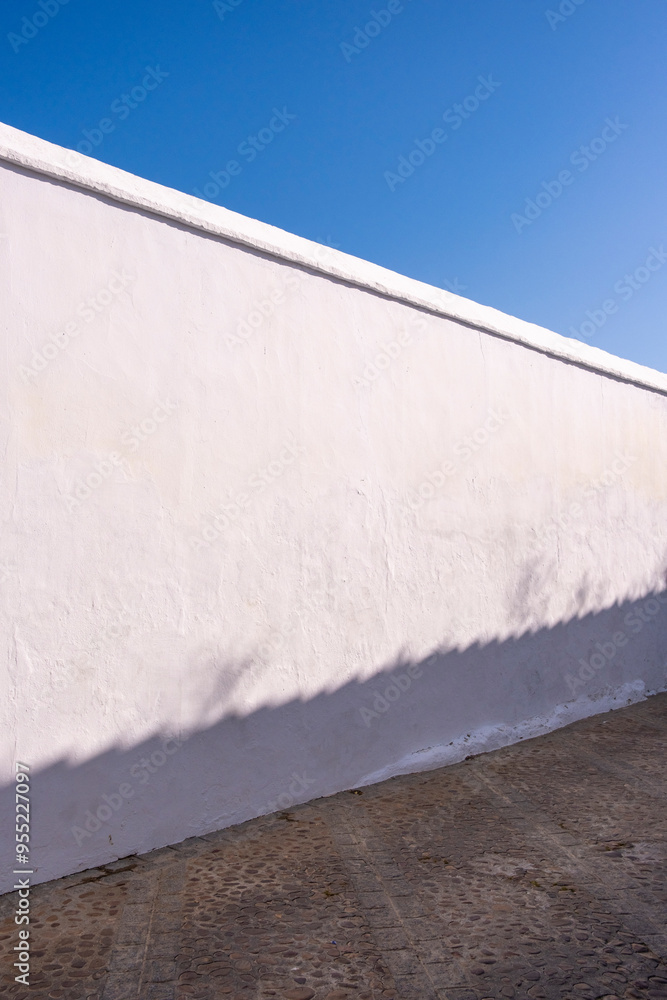 © yaqui_villegas - Minimalist capture of a white wall casting its shadow onto a cobblestone path, exemplifying simplicity and geometric balance in urban architecture in Carmona Andalusia Spain
