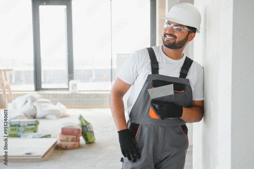 Indian Male builder in work overalls plastering a wall using a construction trowel. Indian Male builder in work overalls plastering a wall using a construction trowel.