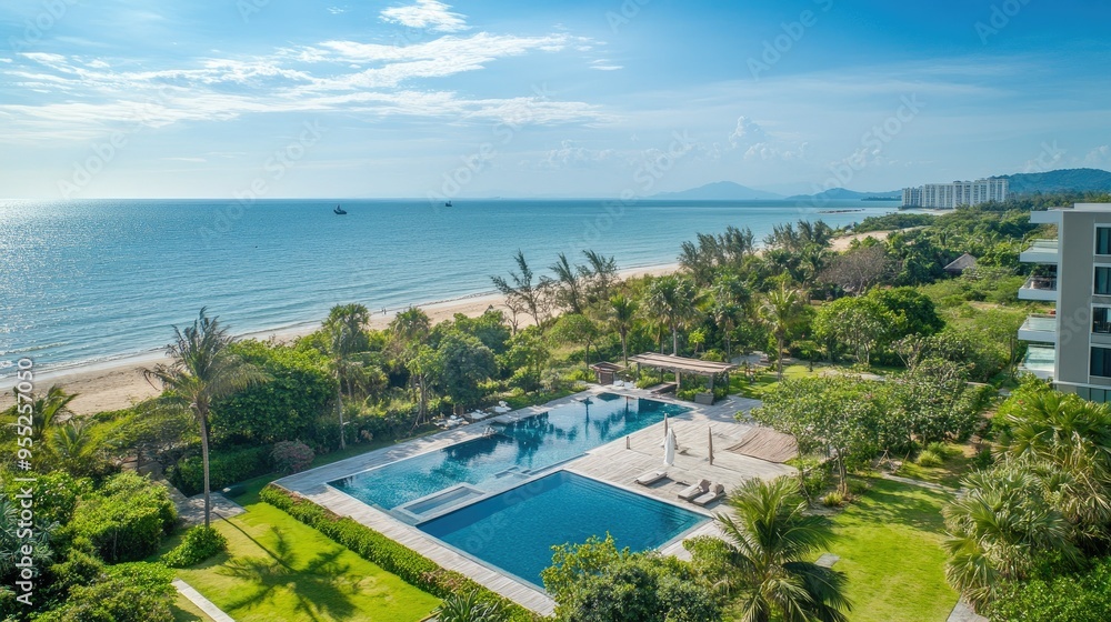 Fototapeta premium Aerial view of a serviced condominium for rent in Hua Hin, featuring a swimming pool, tropical greenery, and stunning views of the sea and beach under a sunny sky