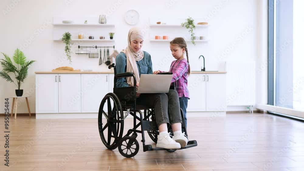 Mother in wheelchair and daughter using laptop together in modern kitchen. Happy family moments filled with learning and bonding. Bright, airy interior showcases accessibility and inclusivity.