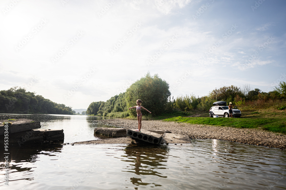 Child balancing on pier by riverside with parked car nearby Child balancing on pier by riverside with parked car nearby