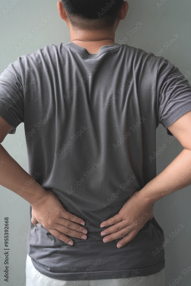 Close up young asian man hold his pained back from work isolated on grey background. Office syndrome, disease, illness, sick, muscle pain, overwork, wrist ache, arm hurt and arthritis concept. Close up young asian man hold his pained back from work isolated on grey background. Office syndrome, disease, illness, sick, muscle pain, overwork, wrist ache, arm hurt and arthritis concept.