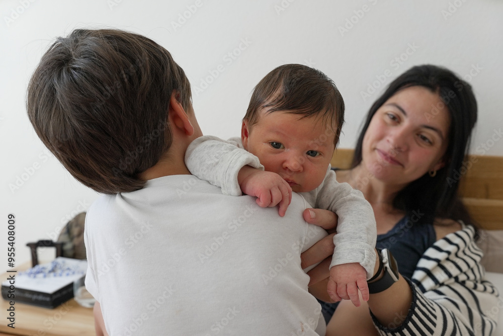 Newborn baby being held by older brother with mother watching, capturing a tender family moment of sibling bonding and parental love, perfect for family and childhood themes Newborn baby being held by older brother with mother watching, capturing a tender family moment of sibling bonding and parental love, perfect for family and childhood themes