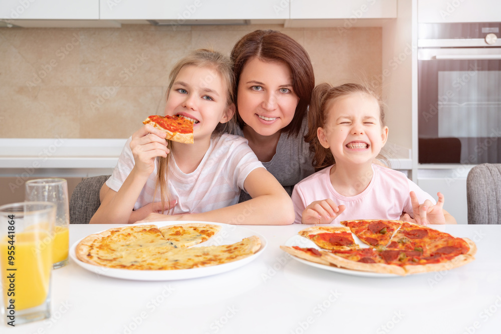Mother and two daughters eating homemade pizza at a table in kitchen, happy family concept Mother and two daughters eating homemade pizza at a table in kitchen, happy family concept