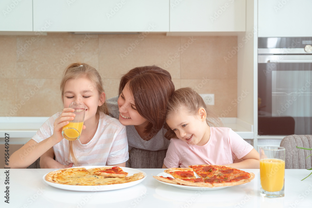 Mother and two daughters eating homemade pizza at a table in kitchen, happy family concept Mother and two daughters eating homemade pizza at a table in kitchen, happy family concept