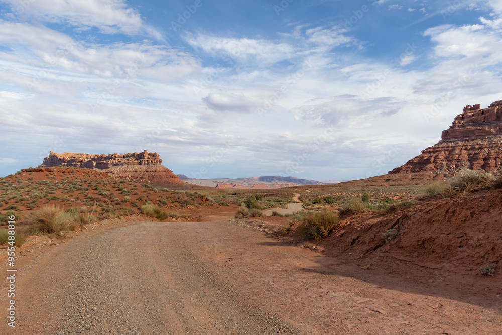 A dirt road leading through Valley of the Gods in Utah with red rocks and open desert. A dirt road leading through Valley of the Gods in Utah with red rocks and open desert.