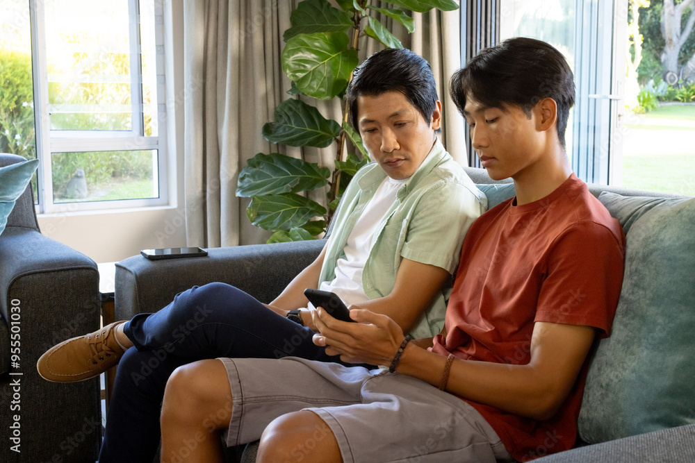 Sitting on couch, father and son looking at smartphone together at home Sitting on couch, father and son looking at smartphone together at home