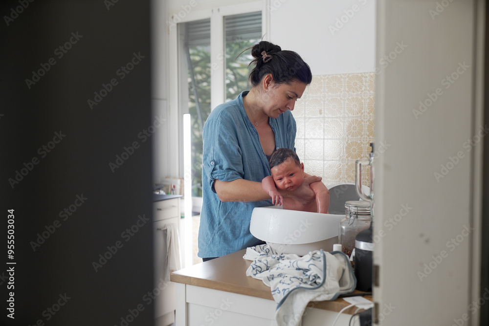 Mother bathing newborn in baby bathtub in kitchen, indoor scene, baby looking calm, maternal care, nurturing moment, home environment, hygiene routine, parental bonding, infant bathing Mother bathing newborn in baby bathtub in kitchen, indoor scene, baby looking calm, maternal care, nurturing moment, home environment, hygiene routine, parental bonding, infant bathing