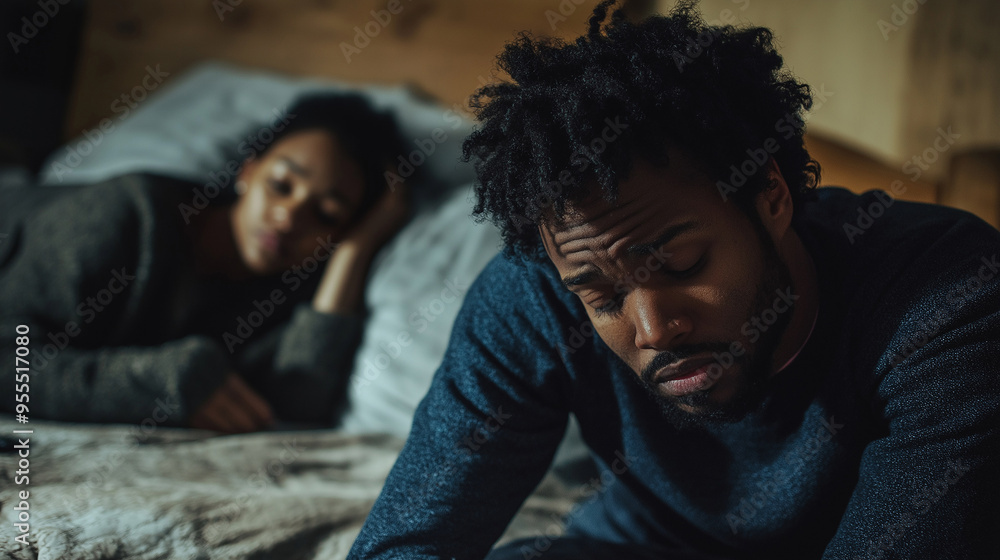 Obraz premium Young man feeling sad while woman is lying in bed in the background