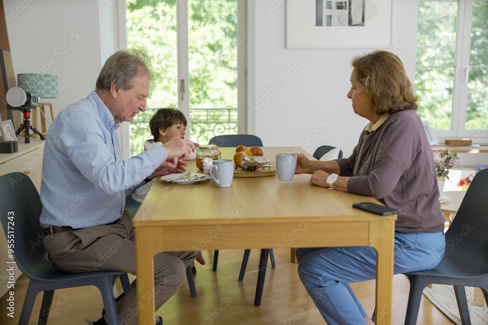 Older couple and young child enjoy breakfast together at a dining table, illustrating a multi-generational family bond and sharing a simple, joyful moment in a bright, cozy home Older couple and young child enjoy breakfast together at a dining table, illustrating a multi-generational family bond and sharing a simple, joyful moment in a bright, cozy home
