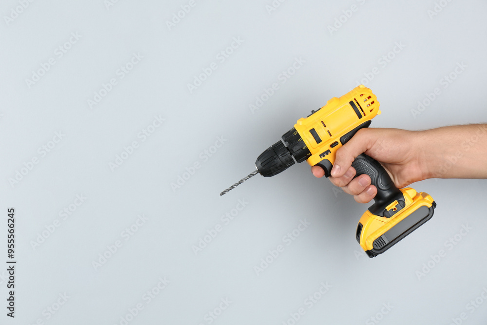 Man with cordless electric drill on light grey background, closeup. Space for text Man with cordless electric drill on light grey background, closeup. Space for text