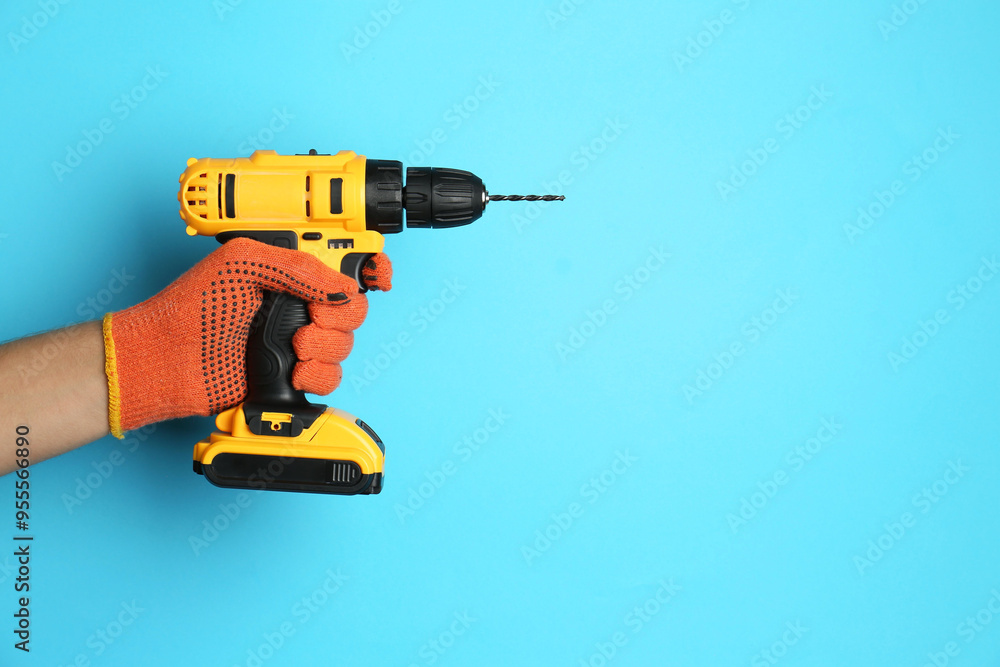 Man with cordless electric drill on light blue background, closeup. Space for text Man with cordless electric drill on light blue background, closeup. Space for text