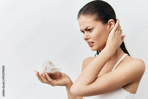 Hair loss struggle, woman with detached hair in hand, exhibiting concern and frustration, neutral background The image captures an emotional moment related to beauty and self image photo