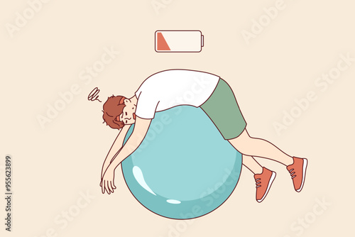 Tired man lies on fitness ball with empty battery, symbolizing exhaustion and lack of vitality. Tired guy being lazy doing pilates to improve health or get rid of illnesses and excess weight