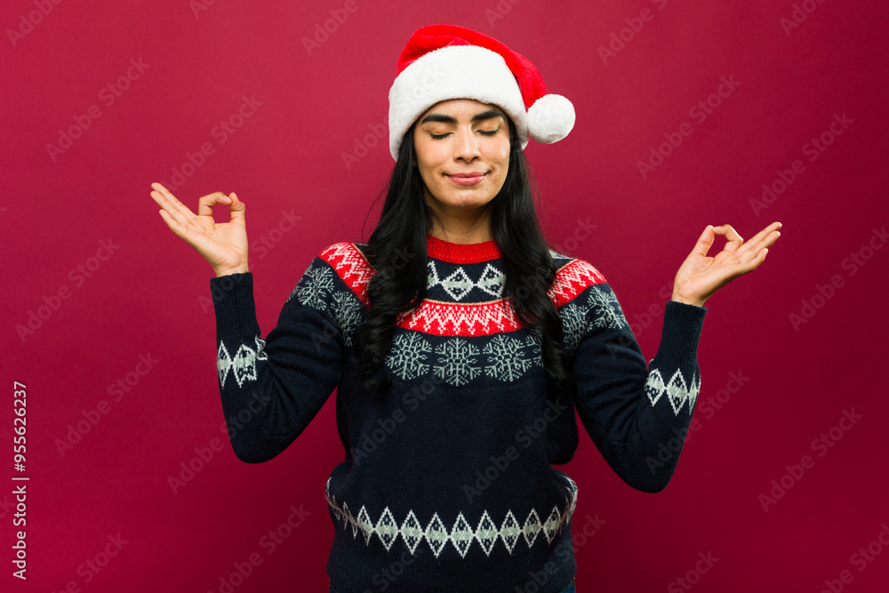 Young hispanic woman wearing a christmas sweater and santa hat meditating, making zen gesture with her hands, keeping eyes closed, over red background Young hispanic woman wearing a christmas sweater and santa hat meditating, making zen gesture with her hands, keeping eyes closed, over red background