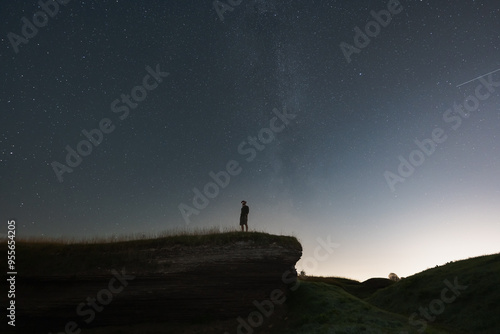 Night scene, a man with a night vision device stands on a cliff. The starry sky and the milky way.